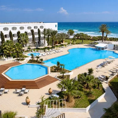 Vue panoramique des grandes piscines extérieures, des transats et du bâtiment blanc du Mondi Club Thalassa Mahdia au bord de la mer.