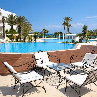 Espace détente avec fauteuils en fer forgé et coussins blancs au bord de la piscine de l'hôtel Mondi Club Thalassa Mahdia.