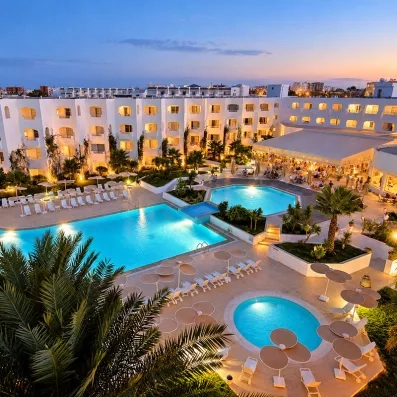Vue nocturne éclairée des piscines extérieures et de la façade de l'hôtel Mondi Club Thalassa Mahdia en Tunisie.