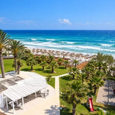 Vue aérienne du jardin arboré de palmiers, des équipements de loisirs et de la plage de sable du Mondi Club Thalassa Mahdia.