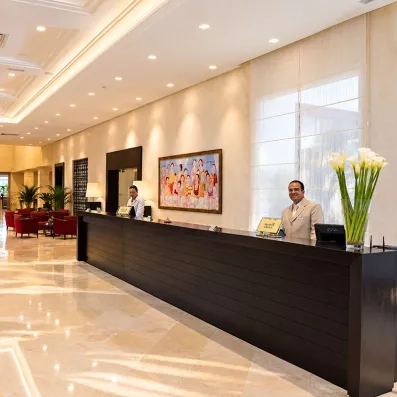 Comptoir de réception en bois foncé de l'hôtel Mondi Club Thalassa Mahdia avec le personnel d'accueil souriant.