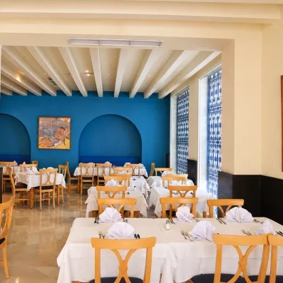 Salle de restaurant lumineuse de l'hôtel Mondi Club Thalassa Mahdia avec tables dressées et murs bleus style méditerranéen.