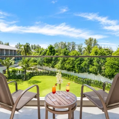 Un balcon avec une table et deux chaises, offrant une vue face à un jardin.
