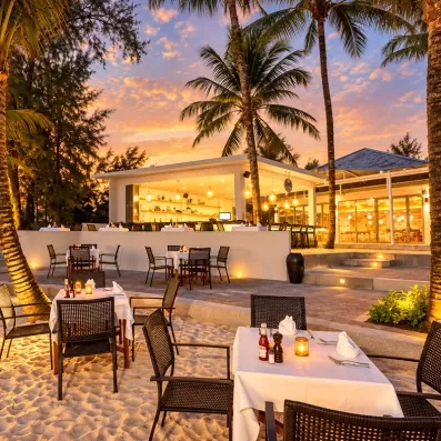 Un dîner en terrasse sur le sable, avec des tables dressées sous les palmiers.