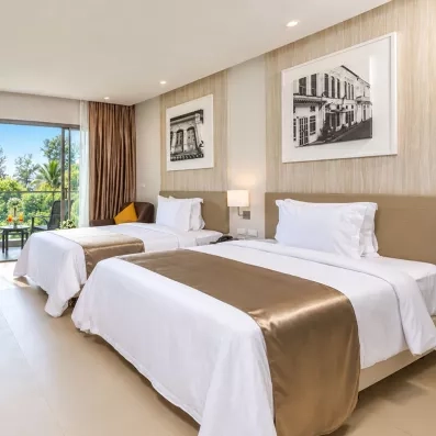 Une chambre d'hôtel avec deux lits doubles, s'ouvrant sur un balcon avec vue sur la verdure.
