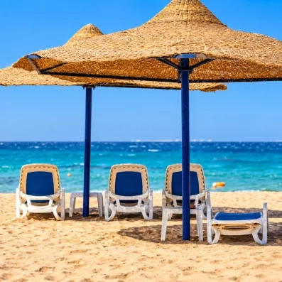 Transats et parasols en paille sur la plage de sable avec vue sur la mer à l'hôtel Blend Club Aqua Resort Hurghada.