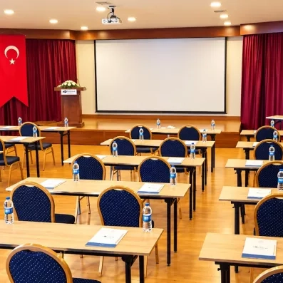 Une salle de conférence aménagée avec des tables en bois, des chaises et un écran.
