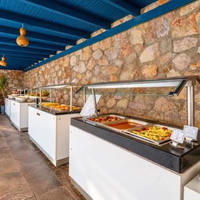 Un long buffet de plats chauds présenté sous des lampes chauffantes devant un mur en pierre rustique.