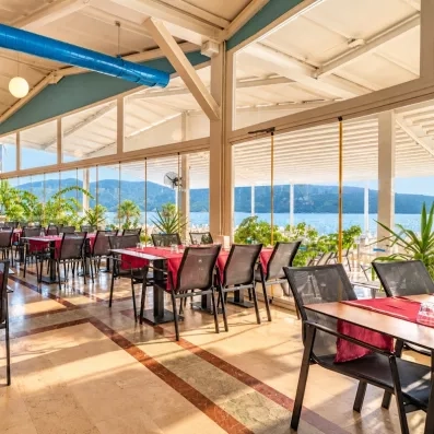 Une vaste salle de restaurant intérieure lumineuse avec des tables dressées et de grandes baies vitrées.