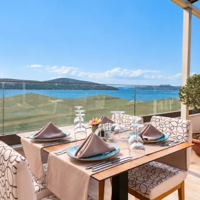 Une table de restaurant dressée sur un balcon, capturant un magnifique coucher de soleil sur la baie.
