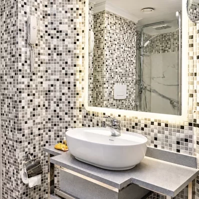 Salle de bain moderne avec mosaïque et grand miroir lumineux dans une cabine de croisière chic.
