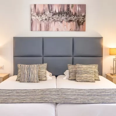 Chambre double confortable avec tête de lit capitonnée grise au complexe hôtelier César Thalasso à Djerba.