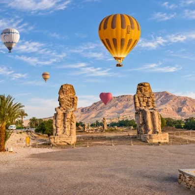 Colosses de Memnon survolés par des montgolfières à l'aube, excursion touristique emblématique en Haute-Égypte.