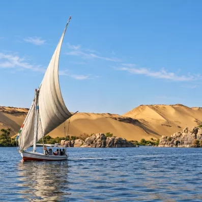 Felouque traditionnelle naviguant sur le Nil devant les dunes de sable d'Assouan, voyage authentique en Égypte.
