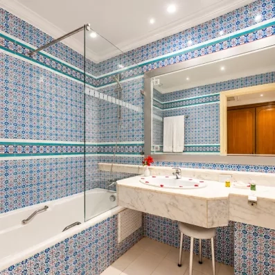 Salle de bain typique à l'hôtel Djerba Golf avec carrelage mosaïque bleu, marbre et baignoire moderne.