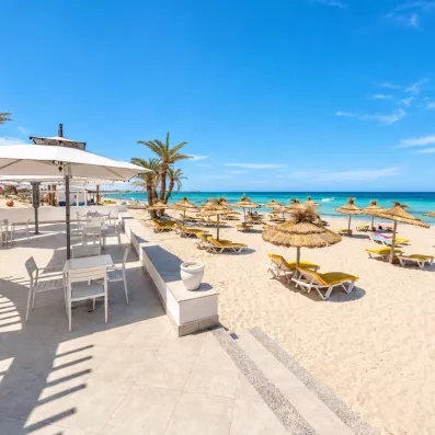 Plage de sable fin aménagée avec transats et parasols traditionnels sous le soleil de Djerba.