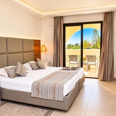 Chambre double moderne de l'hôtel Djerba Aqua Resort avec grand lit et balcon aménagé donnant sur le jardin.