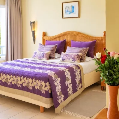 Détail d'un lit double élégant au Djerba Resort avec tête de lit en osier et fleurs fraîches.