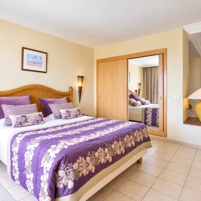 Suite spacieuse du Djerba Resort avec grand lit double, décoration violette et grand miroir intégré.