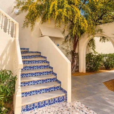 Escalier extérieur orné de mosaïques bleues traditionnelles sous une glycine jaune au César Thalasso Djerba.