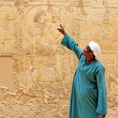 Guide local en tenue traditionnelle expliquant des bas-reliefs antiques lors d'une croisière à Louxor, Égypte.