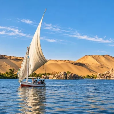 Felouque traditionnelle naviguant sur les eaux bleues du Nil devant des dunes de sable d'Égypte au soleil.