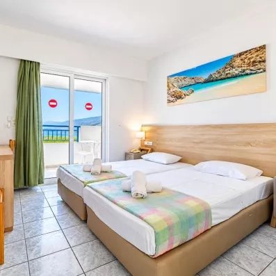 Chambre avec deux lits collés, une tête de lit en bois, un tableau d'une plage et une porte fenêtre de la terrasse