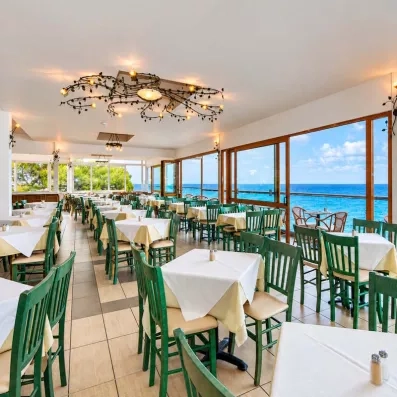 salle de restaurant donnant sur la plage avec des chaises vertes en bois et des tables dressées