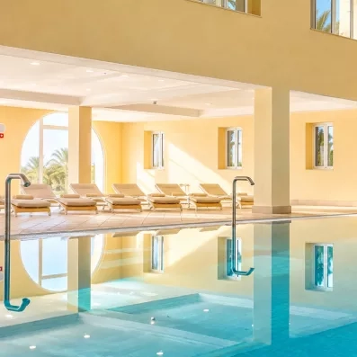 Chaises longues alignées au bord d'une piscine intérieure lumineuse pour un séjour bien-être à Djerba.