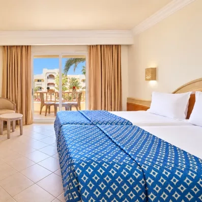 Chambre lumineuse avec balcon vue sur piscine et palmiers à l'hôtel Les Quatre Saisons à Djerba, Tunisie.