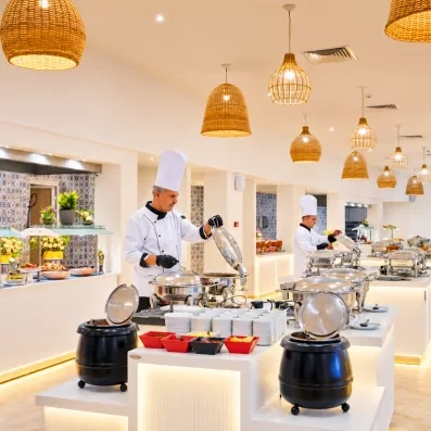 Chefs cuisiniers préparant des plats chauds en buffet sous des luminaires en osier à Djerba.