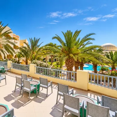 Terrasse panoramique ensoleillée avec fauteuils confortables bordée de palmiers sous le ciel bleu de Djerba.