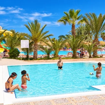 Enfants s'amusant dans le pataugeoire de l'hôtel Les Quatre Saisons sous les palmiers.