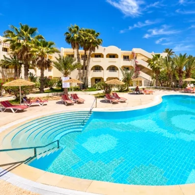 Piscine extérieure de l'hôtel les quatre saisons étincelante bordée de parasols en paille et palmiers pour un séjour détente à Djerba.