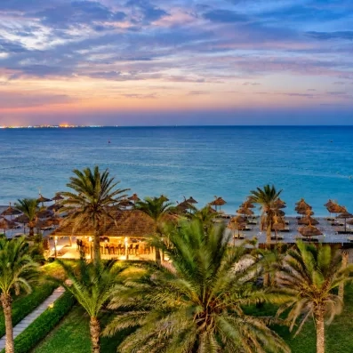 Bar de plage éclairé au crépuscule sous les palmiers face à la mer à l'hôtel Royal Thalassa.