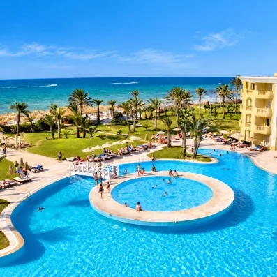 Grande piscine extérieure avec îlot central, palmiers et vue sur mer Méditerranée au Royal Thalassa Monastir.