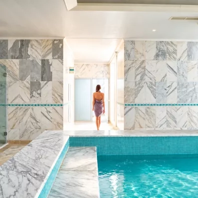 Femme en drap de bain marchant vers un bassin de thalasso en marbre au Royal Thalassa Monastir.