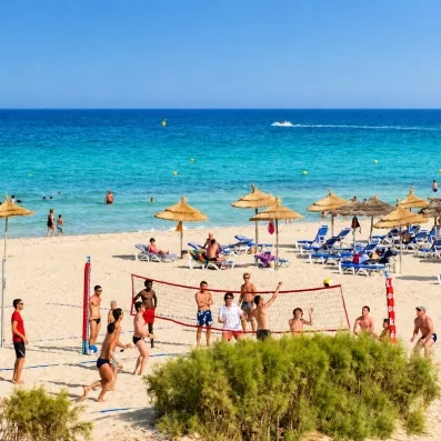 Panorama de la plage privée avec clients jouant au beach volley de l'hôtel Helios Beach.
