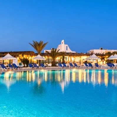piscine illuminée de nuit avec rangée de transats et parasols et façade de l'hôtel helios beach à djerba en tunisie