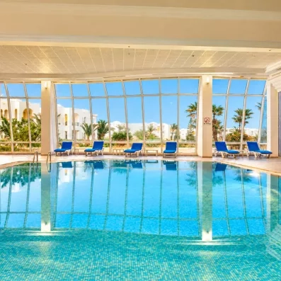 Piscine intérieure chauffée avec vue panoramique sur les jardins de l'hôtel Helios Beach à Djerba.