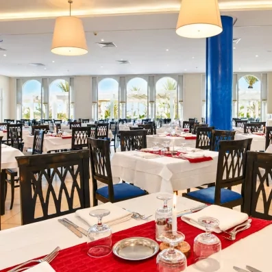 Tables dressées avec élégance dans la salle de restaurant lumineuse de l'hôtel Helios Beach à Djerba.