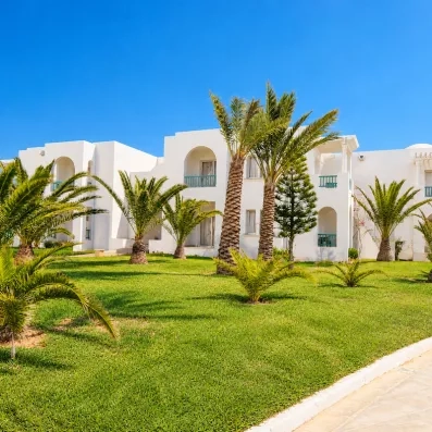 Architecture traditionnelle tunisienne et palmiers exotiques dans les jardins ensoleillés de l'hôtel Helios Beach à Djerba.