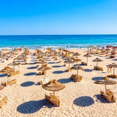 Une plage de sable fin bordée de parasols en paille, avec vue sur une mer turquoise, pour se détendre au soleil.