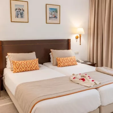 Une chambre lumineuse aux tons chaleureux, avec deux lits confortables et une décoration soignée aux touches orangées.