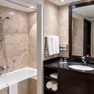 Une salle de bain habillée de marbre beige, équipée d'une baignoire, d'une vasque et d'un grand miroir, pour un moment de détente tout confort.