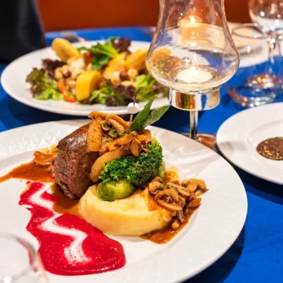 Un plat soigné mêlant viande, légumes et purée, accompagné d'une salade et d'un dessert, pour une expérience culinaire raffinée.