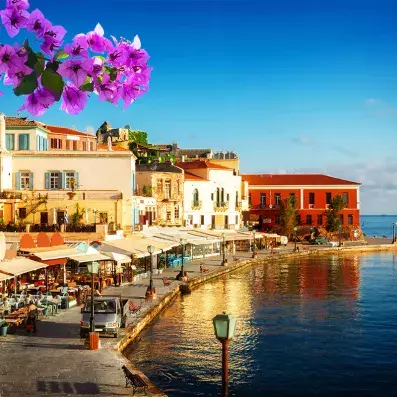 Port de La Canée en Crète avec façades colorées, terrasses de cafés en bord de mer et bougainvilliers au soleil couchant.