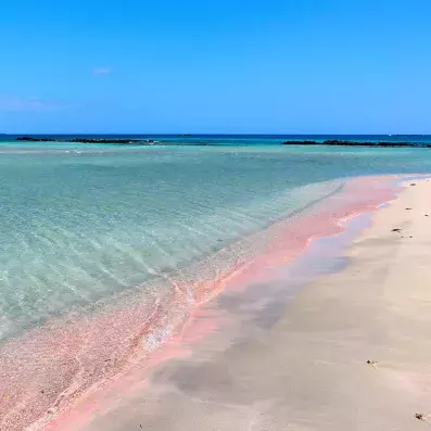 Plage d’Elafonissi en Crète avec sable rosé, eau turquoise peu profonde et lagon protégé, paysage paradisiaque.