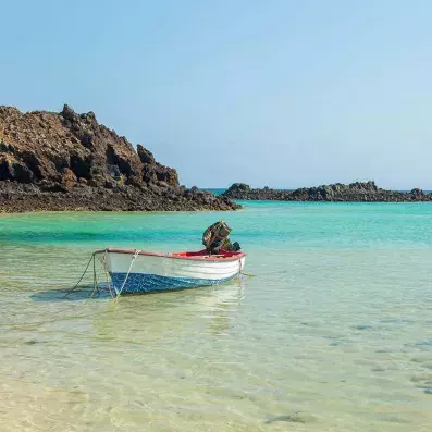 Petit bateau sur eau turquoise près de l’île de Lobos à Fuerteventura, lagon cristallin, rochers volcaniques et ciel clair.
