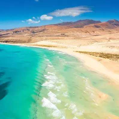 Dunes et lagon du parc naturel de Corralejo à Fuerteventura, plage de sable clair, eau turquoise et reliefs volcaniques.